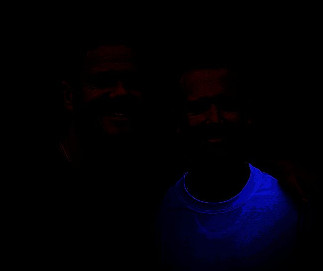 Dan与Mac兄弟合影，身穿休闲装，背景为游戏开发工作室，桌上摆放着《Last Flag》相关模型和宣传海报