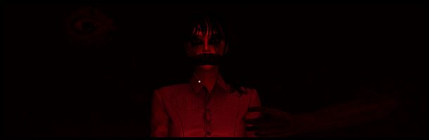 艾玛站在旅馆走廊尽头，身后是黑暗的房间，前方光线微弱，营造出紧张氛围