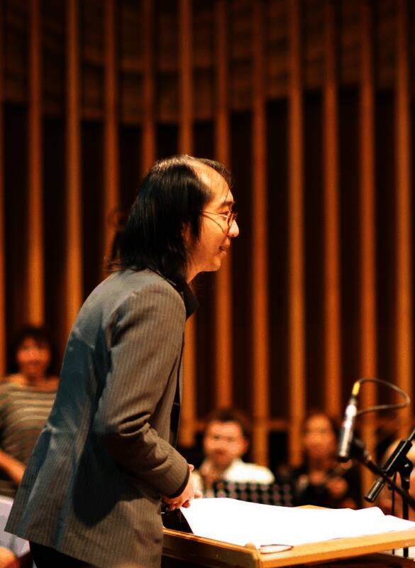 日本著名作曲家久保田修正在录音室工作画面，身旁摆满乐谱和设备