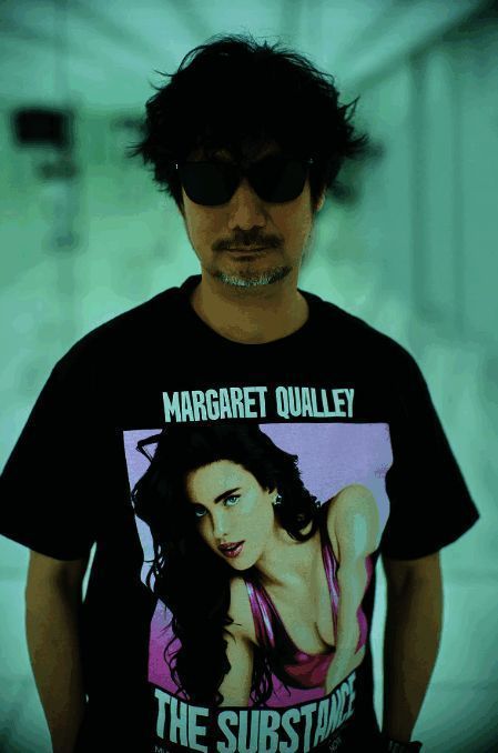 小岛秀夫身穿《某种物质》联名T恤，神情冷峻，背景为电影海报