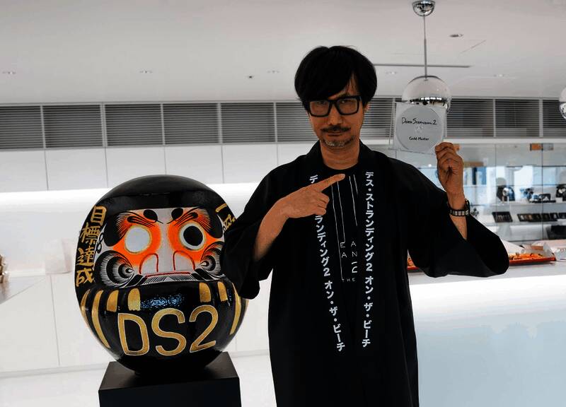 《死亡搁浅2》游戏实机画面展示主角Sam穿越沙漠地带，背景可见标志性机械装置