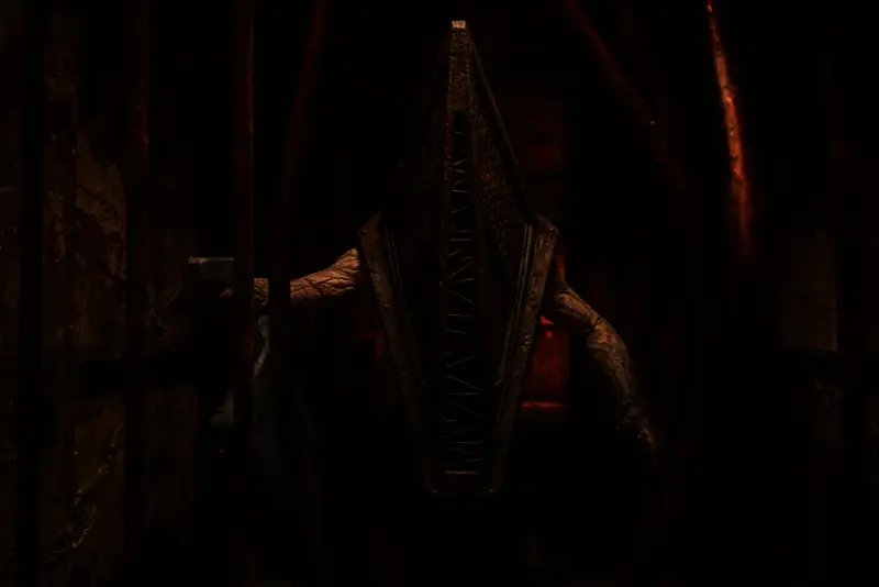 《重返寂静岭》电影海报，画面中心为标志性的三角头怪物轮廓，背景是血红色天空