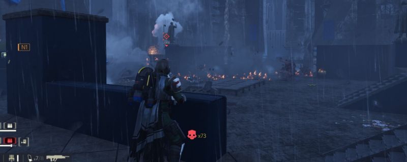 《绝地潜兵2》中角色正在进行贴地滑铲动作，身体低伏向前疾行，背景为激烈的战场环境，子弹轨迹与爆炸特效环绕