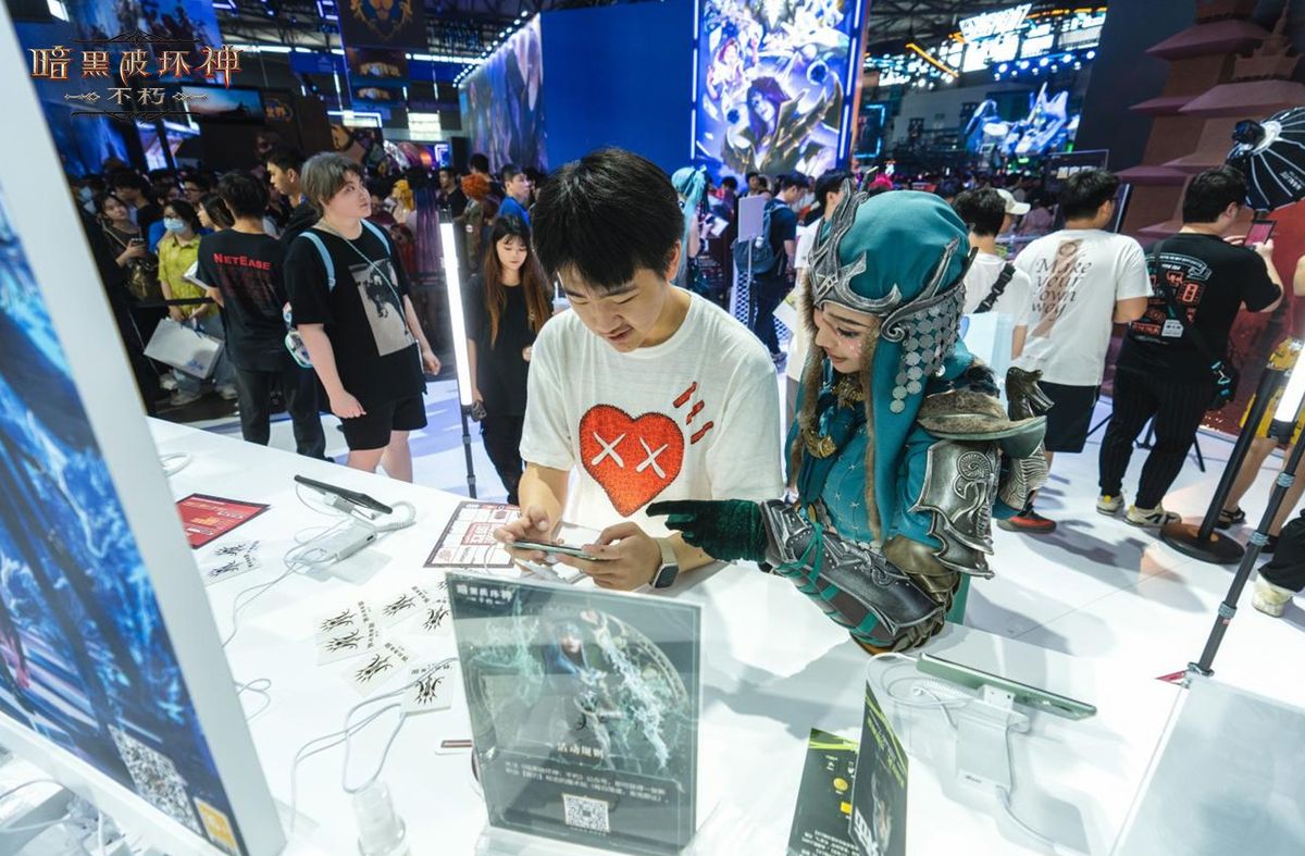 玩家在展台试玩《暗黑破坏神：不朽》，屏幕上显示雾刃战斗画面，工作人员在一旁协助