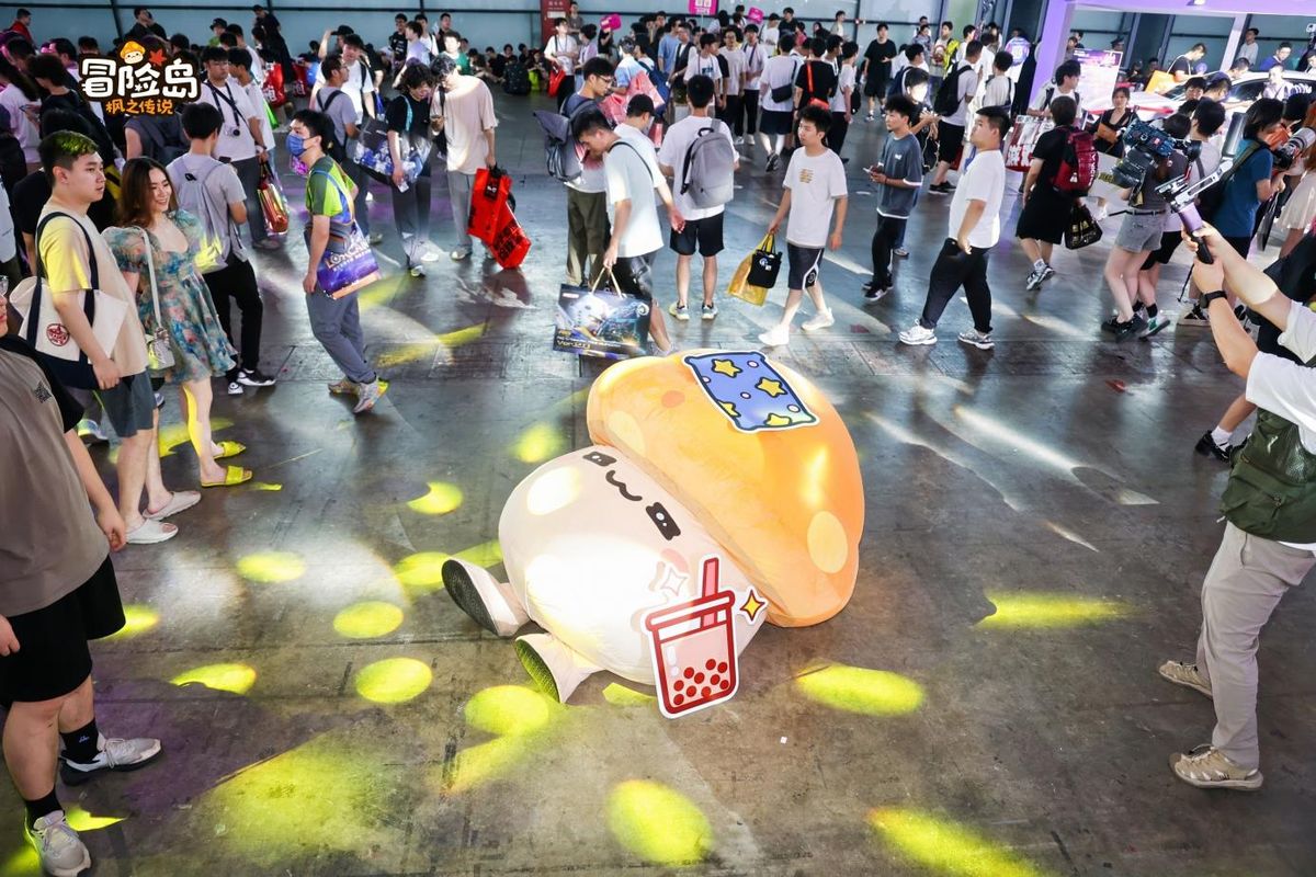 《冒险岛：枫之传说》展区中，花蘑菇和企鹅王造型的NPC躺在展台角落，姿态放松，周围玩家纷纷拍照互动