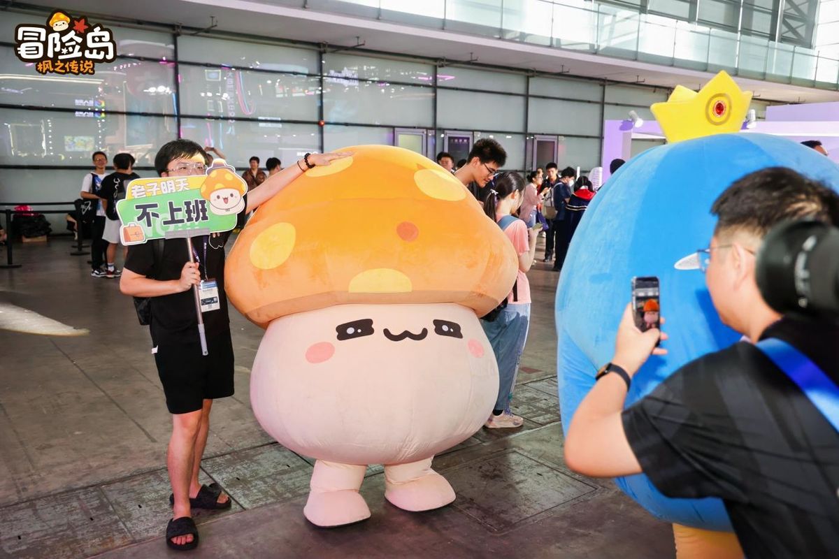 企鹅王NPC与多位玩家在展区前合影，背景为巨大的游戏LOGO灯牌