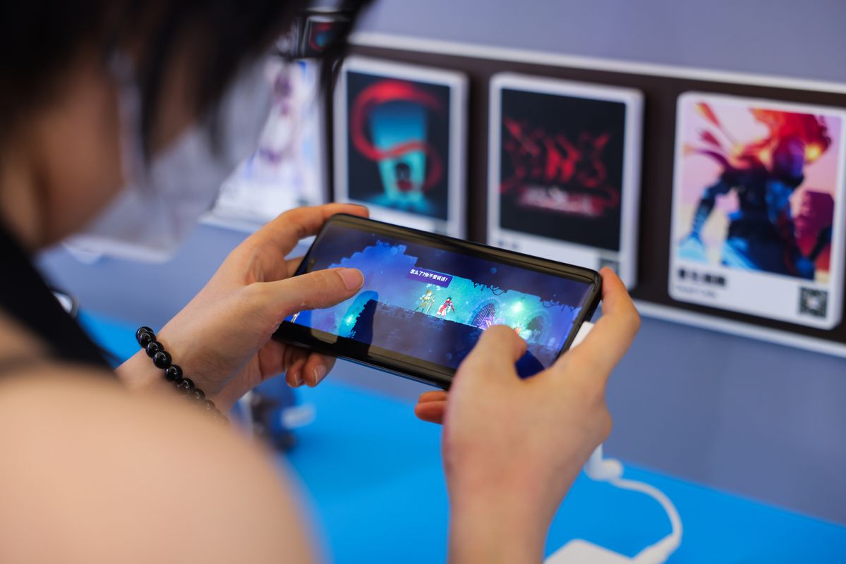 玩家手持荣耀Magic V3专注试玩游戏，背景为展台炫彩灯光与游戏海报