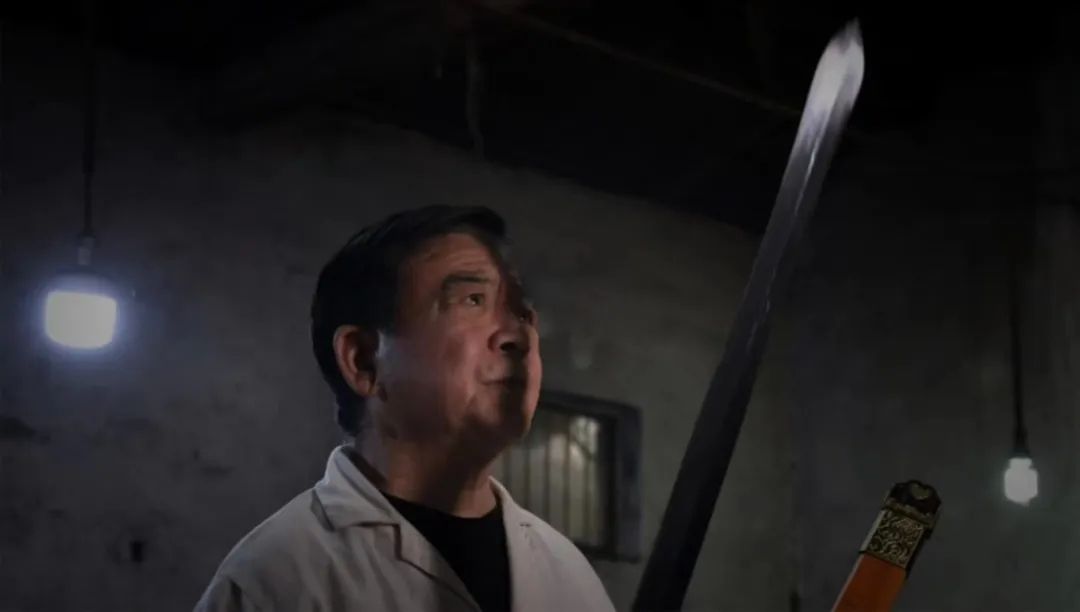 高庆民老师手持棠溪宝剑，身穿传统工匠服饰，神情专注