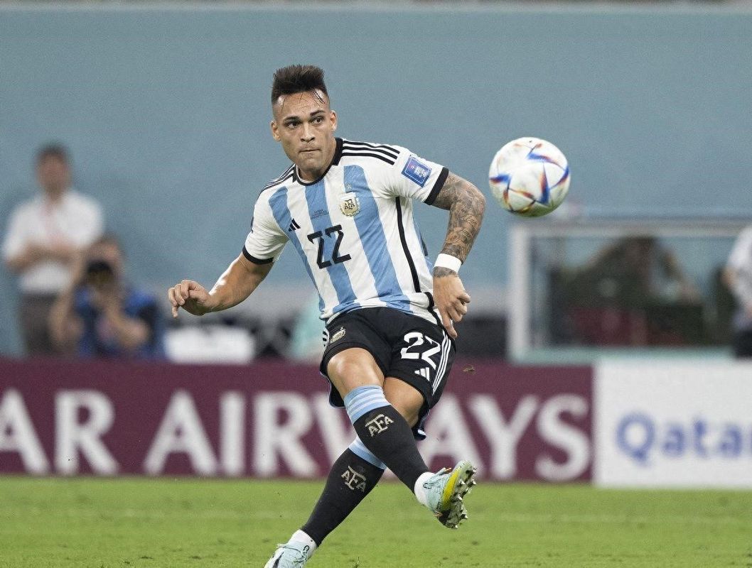 劳塔罗·马丁内斯身穿阿根廷国家队球衣，在球场上激情庆祝进球，背景是沸腾的球迷看台