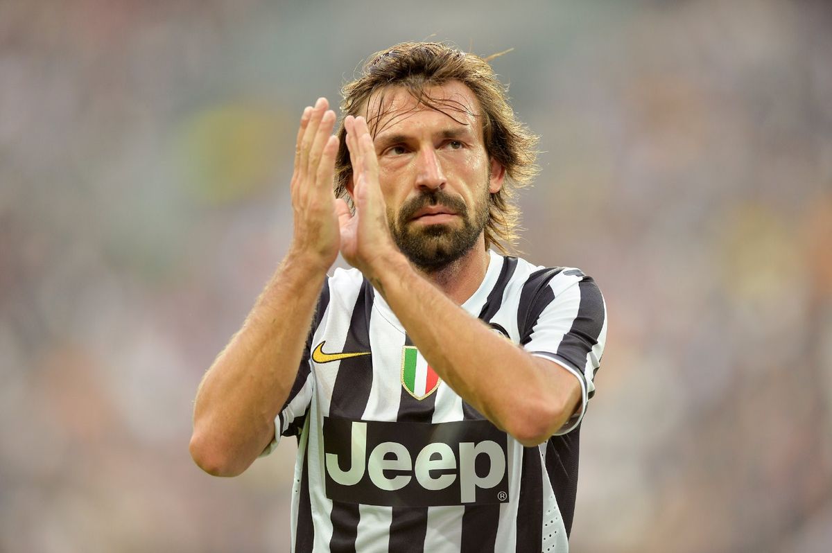 安德烈亚·皮尔洛身穿尤文图斯球衣，站在球场中央沉思，背景是热烈的球迷看台