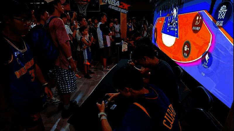 一名玩家戴着巨型篮球手套尝试投篮，表情滑稽，周围观众大笑鼓掌