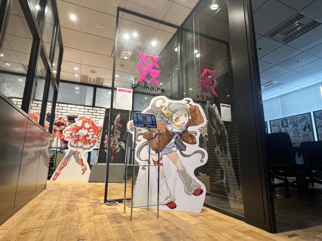Grimoire办公室内部场景，墙上贴满角色原画与手写标语，桌上摆放着动漫模型和开发用笔记本，氛围充满创作激情