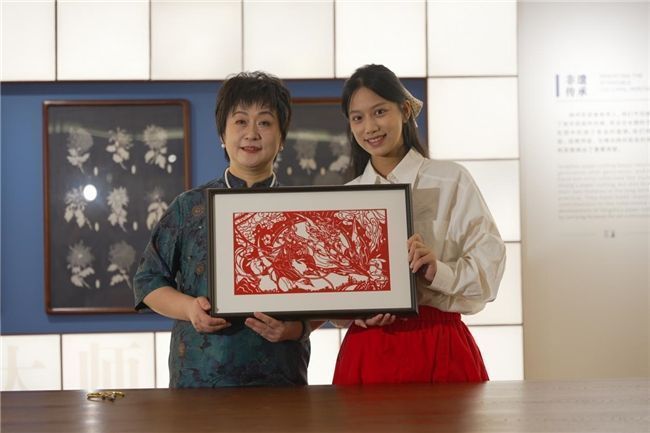 现场观众参与剪纸互动体验，年轻玩家在指导下亲手制作《指间山海》角色剪纸，神情专注