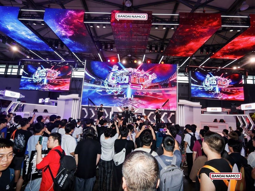 万代南梦宫展区全景图，展台设计融合多种游戏元素，灯光璀璨，人潮涌动