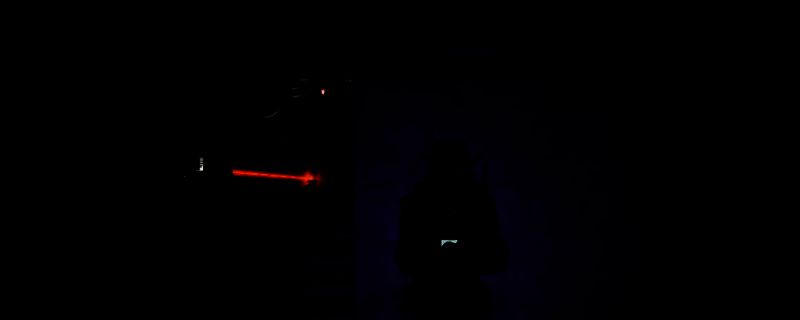 游戏中安保区死神怪物被X射线照射的场景，角色手持设备对准静止的敌对生物，周围漂浮着暗影精华