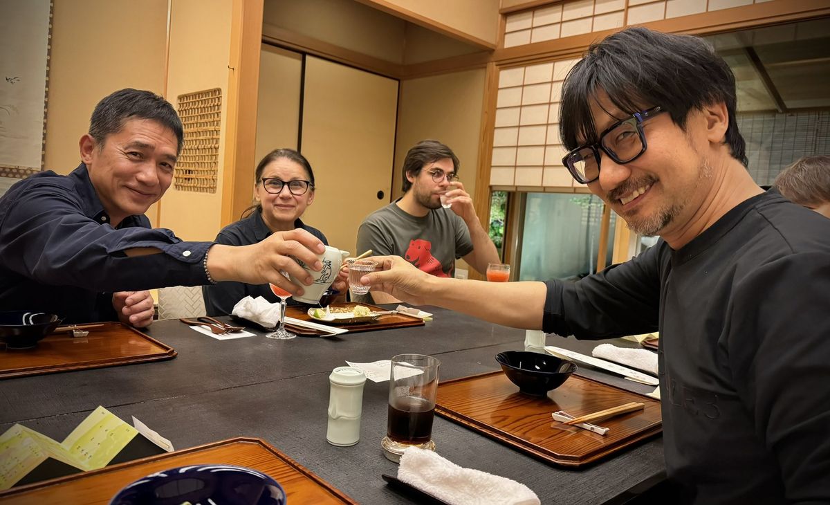 小岛秀夫与嘉宾们围坐交谈，桌上摆放多份文件与模型