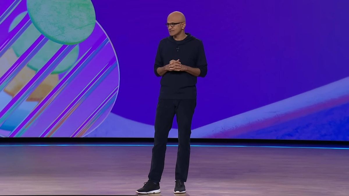 微软CEO萨蒂亚·纳德拉在演讲中神情专注，背景为微软标志与Xbox游戏画面