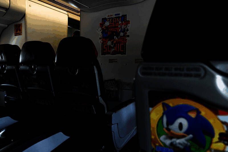 乘客在机场登机口与大型索尼克立牌合影，背景是印有‘Sonic the Hedgehog’字样的主题展板