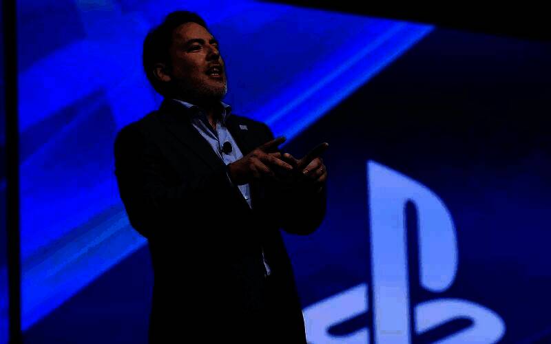 舞台灯光下，Layden手持话筒站在大屏幕前，背景显示着‘The Death of AA Games’字样