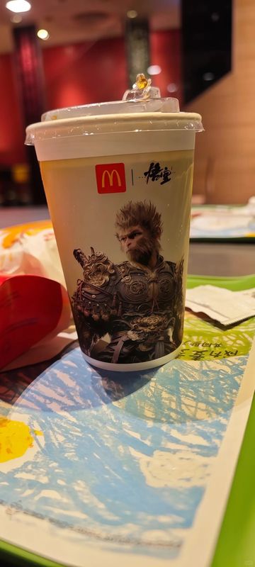 联动概念宣传图，孙悟空手持金箍棒立于麦当劳金色拱门之前，背景为中式云纹与火焰特效交织