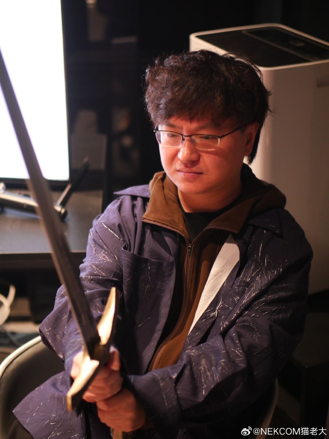 猫老大工作照：手绘风格插画，戴圆框眼镜的卡通形象猫老大伏案于堆满老式录像带、漫画书和赛博朋克海报的桌前，电脑屏幕显示《昭和米国物语》UI界面草稿